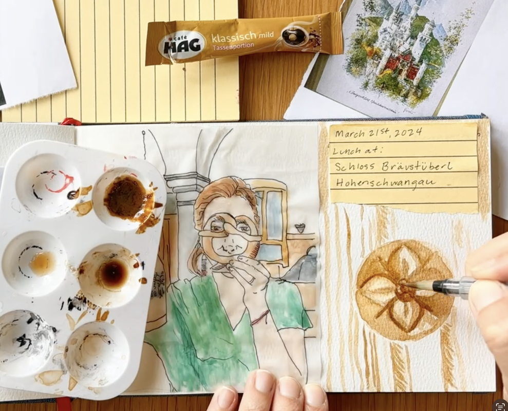 Artist creating a painting of a stylized flower in a travel journal using instant coffee 